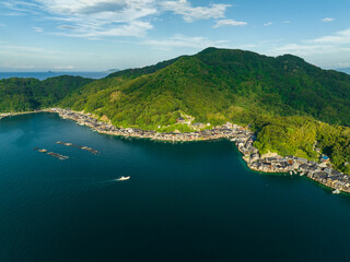 Aerial view of small boat approaching coastal fishing village by mountain