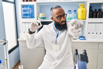 African american man working at scientist laboratory holding syringe pointing with finger to the camera and to you, confident gesture looking serious