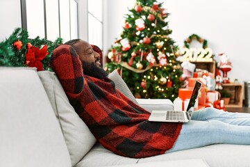 Young african american man relaxed with hands on head sitting by christmas tree at home