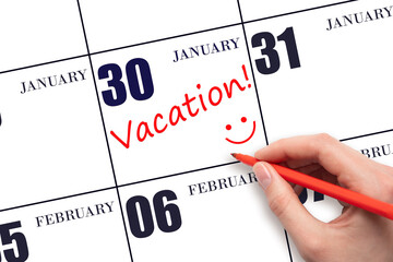 30th day of January. A hand writing a VACATION text and drawing a smiling face on a calendar date 30 January. Vacation planning concept. Winter month, day of the year concept.