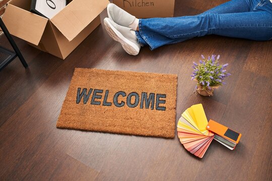 Young blonde woman sittng on the floor near of welcome doormat at new home