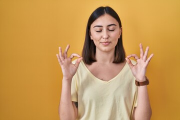 Hispanic girl wearing casual t shirt over yellow background relaxed and smiling with eyes closed doing meditation gesture with fingers. yoga concept.