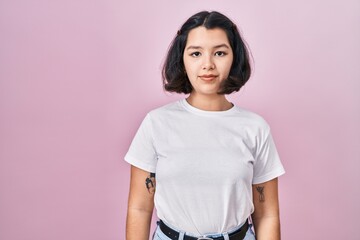 Young hispanic woman wearing casual white t shirt over pink background relaxed with serious expression on face. simple and natural looking at the camera.