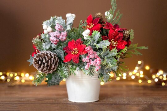 Christmas flower bouquet with red poinsettia, pine cones and spruce branches, festive arrangement on brown background with bokeh lights