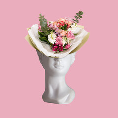 A bouquet of flowers in a vase in the form of female antique statue's head isolated on a pink background. 3d trendy collage in magazine style. Contemporary art. Modern design