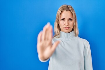 Fototapeta premium Young caucasian woman standing over blue background doing stop sing with palm of the hand. warning expression with negative and serious gesture on the face.