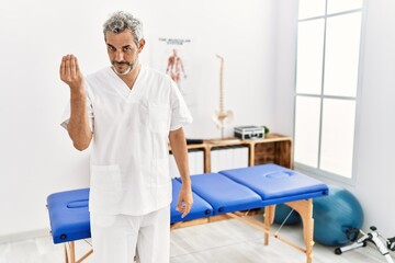 Fototapeta na wymiar Middle age hispanic therapist man working at pain recovery clinic doing italian gesture with hand and fingers confident expression