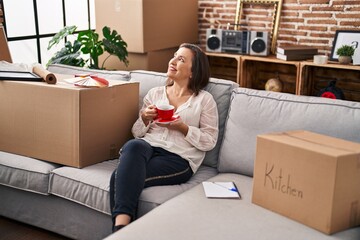 Middle age woman drinking coffee sitting on sofa at new home