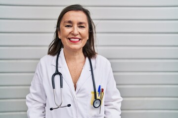 Middle age hispanic woman wearing doctor uniform and stethoscope looking positive and happy standing and smiling with a confident smile showing teeth