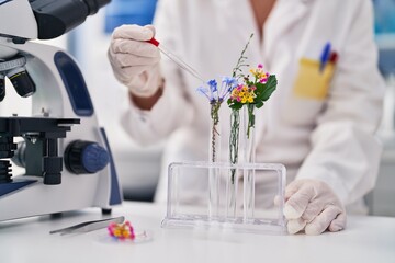 Middle age woman scientist pouring liquid on flower at laboratory