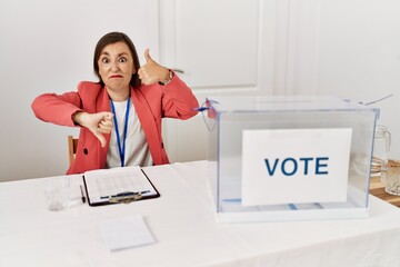 Beautiful middle age hispanic woman at political election sitting by ballot doing thumbs up and down, disagreement and agreement expression. crazy conflict - obrazy, fototapety, plakaty