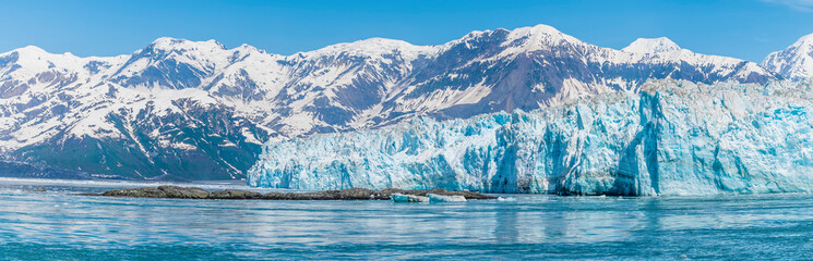 A view past an islet towards the Hubbard Glacier with mountain backdrop in Alaska in summertime