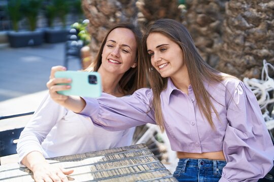 Two women mother and daughter make selfie by smartphone sitting on table at coffee shop terrace