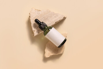 Green glass dropper bottle with blank label lies on beige stones on yellow. Cosmetic Mockup