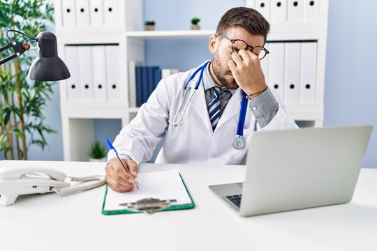 Young hispanic man wearing doctor uniform stressed working at clinic