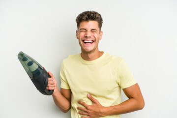 Young caucasian man holding a hand vacuum cleaner isolated on white background laughing and having fun.