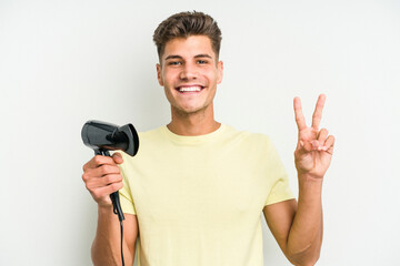 Young caucasian man holding hairdryer isolated on white background showing number two with fingers.