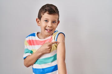 Young caucasian kid getting vaccine showing arm with band aid smiling happy pointing with hand and...