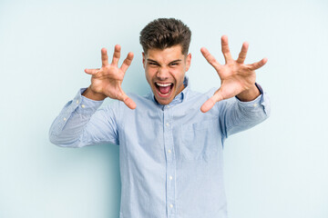 Young caucasian man isolated on blue background showing claws imitating a cat, aggressive gesture.