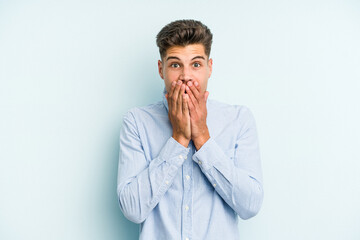 Young caucasian man isolated on blue background shocked, covering mouth with hands, anxious to discover something new.