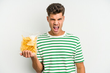 Young caucasian man holding crisps isolated on white background screaming very angry and aggressive.