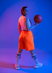 Naklejka premium a girl with a basketball in orange shorts, a t-shirt and a baseball cap. sportswoman in golfs and sneakers on a blue background. Physical education teacher. basketball player