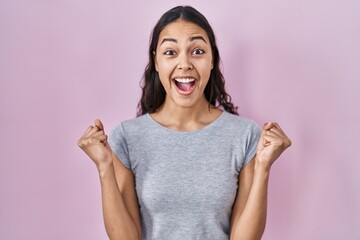 Young brazilian woman wearing casual t shirt over pink background celebrating surprised and amazed for success with arms raised and open eyes. winner concept.