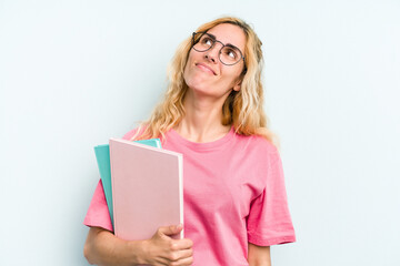 Young student caucasian woman holding books isolated on blue background dreaming of achieving goals and purposes