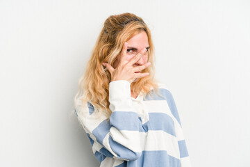 Young caucasian woman isolated on white background blink at the camera through fingers, embarrassed covering face.