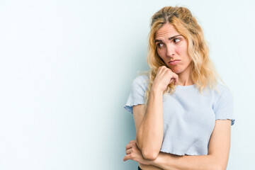 Young caucasian woman isolated on blue background looking sideways with doubtful and skeptical expression.