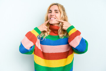 Young caucasian woman isolated on blue background smiles, pointing fingers at mouth.