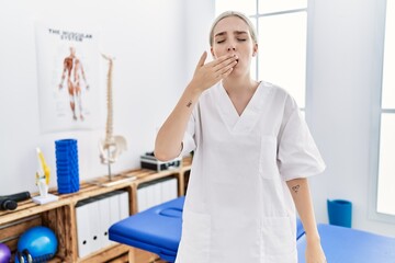 Young caucasian woman working at pain recovery clinic bored yawning tired covering mouth with hand. restless and sleepiness.