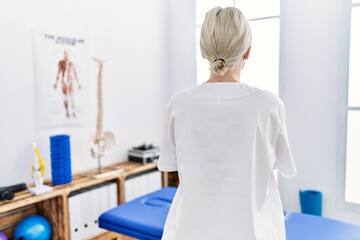 Young caucasian woman working at pain recovery clinic standing backwards looking away with crossed arms