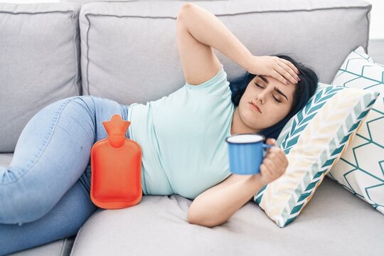 Young caucasian woman suffering for menstrual pain drinking coffee at home