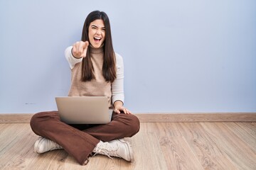 Young brunette woman working using computer laptop sitting on the floor pointing displeased and frustrated to the camera, angry and furious with you