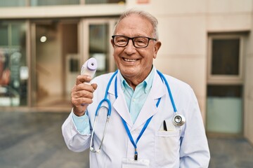 Senior man wearing doctor uniform holding thermometer at street