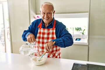 Senior man smiling confident cooking dough at kitchen