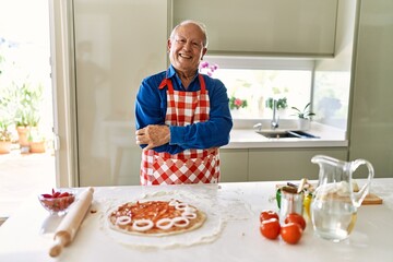Senior man with grey hair cooking pizza at home kitchen happy face smiling with crossed arms looking at the camera. positive person.