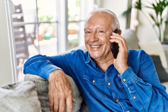 Senior man with grey hair sitting on the sofa at the living room of his house having a conversation speaking on the phone