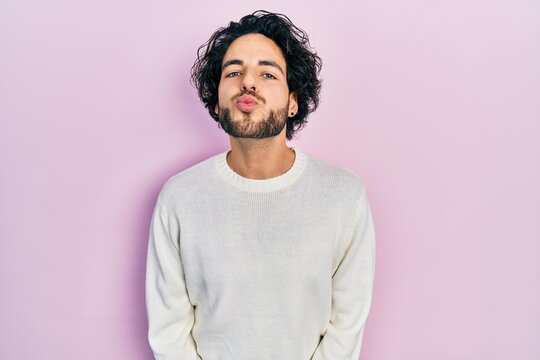 Handsome hispanic man wearing casual white sweater looking at the camera blowing a kiss on air being lovely and sexy. love expression.