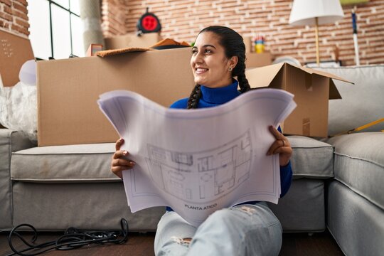 Young hispanic woman smiling confident looking house plans at new home