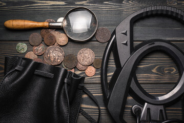 Recreational metal detector and bag full of ancient coins on the wooden table background. Treasure...