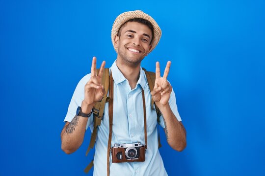 Brazilian young man holding vintage camera smiling looking to the camera showing fingers doing victory sign. number two.
