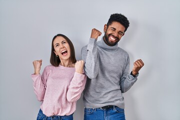 Young hispanic couple standing together celebrating surprised and amazed for success with arms...