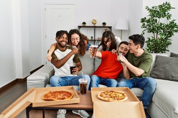 Group of young friends having party eating italian pizza and singing song at home.