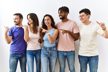 Obraz premium Group of young people standing together over isolated background smiling with happy face looking and pointing to the side with thumb up.