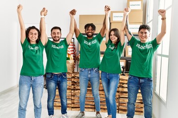 Obraz premium Group of young volunteers smiling happy with hands raised up at charity center.