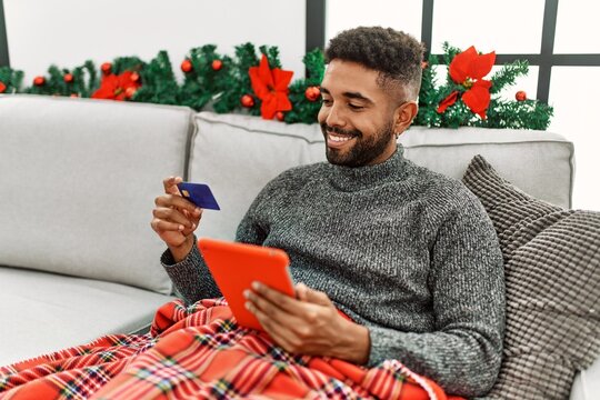 Young african american man smiling happy using laptop and credit card sitting on the sofa at home. - Powered by Adobe