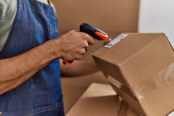 Young hispanic man business worker scanning package using barcode reader machine at storehouse