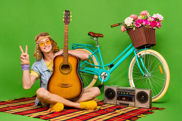 Full length photo of positive hippy guy sit plaid blanket show v-sign isolated on green color background